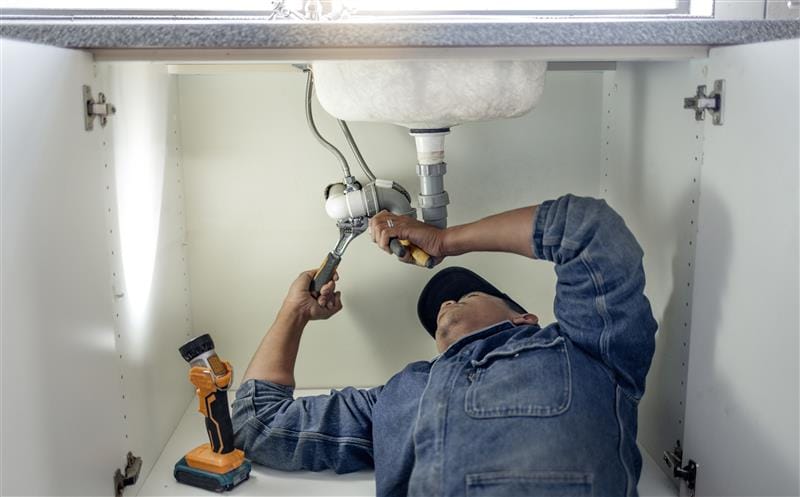 Plumber repairing pipes beneath a bathroom sink in Red Oak
