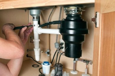 Plumber repairing a garbage disposal beneath a kitchen sink in Red Oak