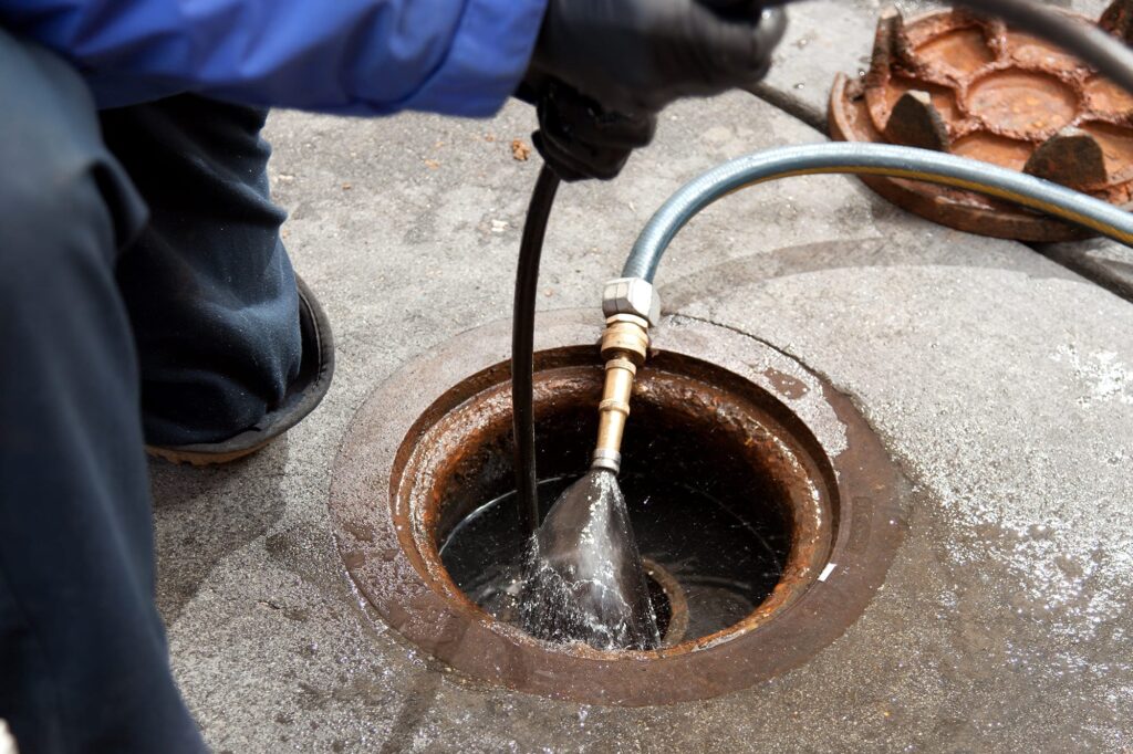 Plumber hydro jetting a sewer line through a manhole in Red Oak