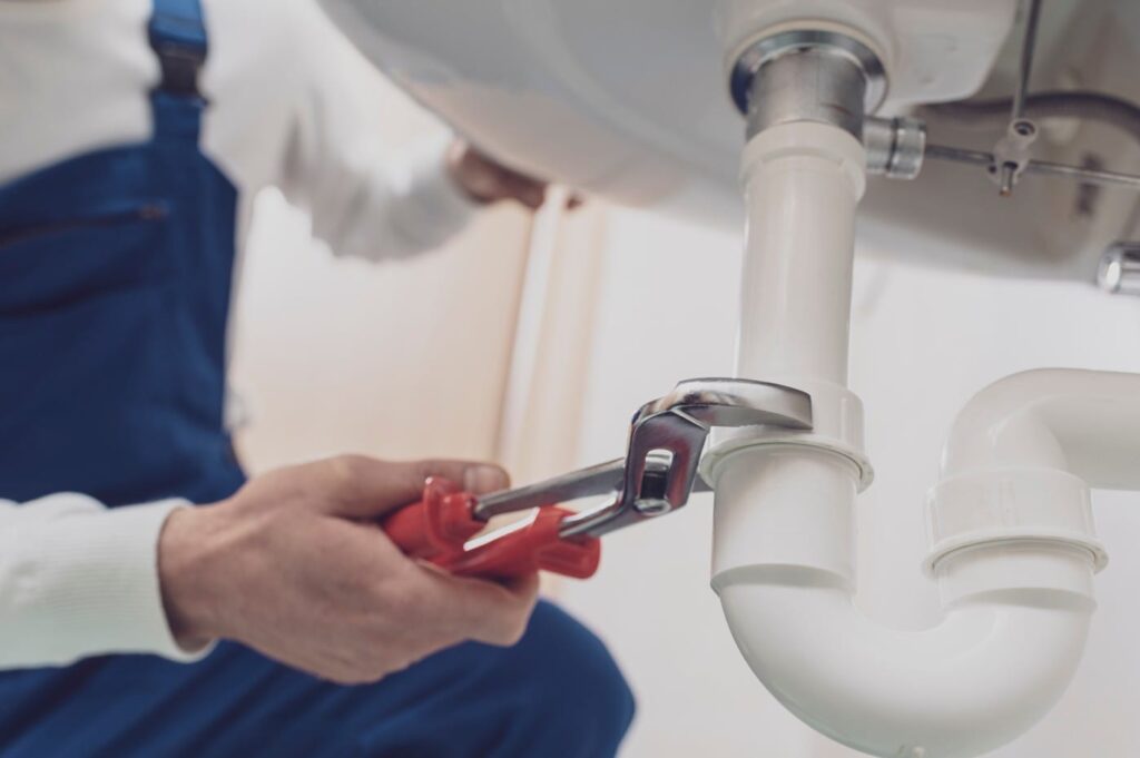 Plumber repairing a white drain pipe beneath a sink in Red Oak