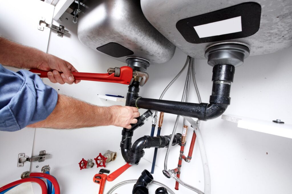 Plumber repairing drain pipes beneath a kitchen sink in Red Oak