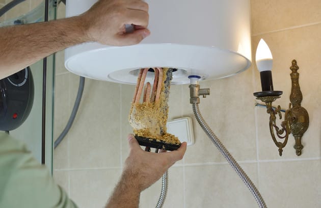 Technician removing mineral buildup from a water heater in Red Oak